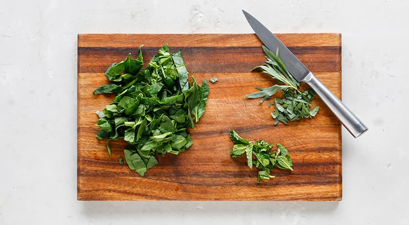 Для приготовления зеленого омлета предварительно разогрейте духовку до 150°С. Грубо порубите шпинат и зелень. Если у зелени (особенно у тархуна и мяты) жесткие стебли, предварительно удалите их.